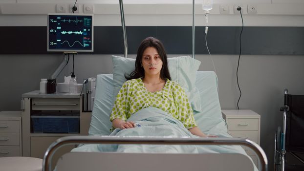 Sick woman with nasal oxygen tube looking into camera resting in bed recovering after respiratory surgery. Patient with breathing disorder waiting for illness treatment in hospital ward