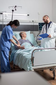 Senior woman laying in hospital bed receiving medication through an intravenous line, discussing with doctor about treatment and diagnosis. Using modern technology for therapy.