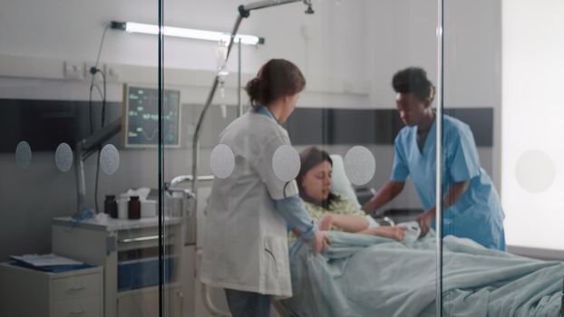 Medical team helping patient putting into bed during sickness emergency monitoring disease symptom checking heartbeat pulse working in hospital ward. Sick woman having respiratory disorder