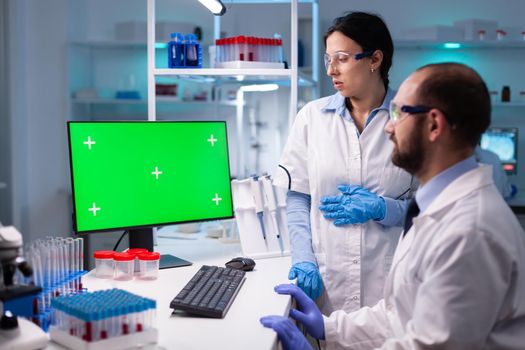 Modern medical research laboratory with two scientists using computer with green chroma key screen. Doctors specialists discovering scientifc experiment with technology equipment industry