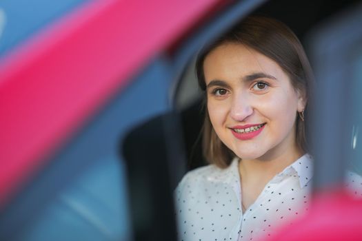 Portrait of Caucasian woman looking through car window to the camera and smiling