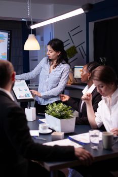 Overworked focused diverse businesspeople working in business company meeting office room brainstorming marketing strategy late at night. Entrepreneur woman presenting financial ideas