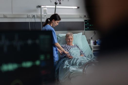 Friendly doctor reassuring sick old patient holding hands, showing emphaty, encouragement, during medical examination in hospital room. Patient breathing through oxygen mask.