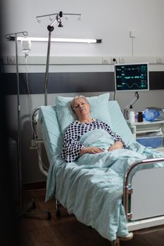 Elderly patient following recovery treatment laying in hospital bed, getting intravenous medicine from iv drip bag. Breathing through oxygen tube because of pulmonary failure.