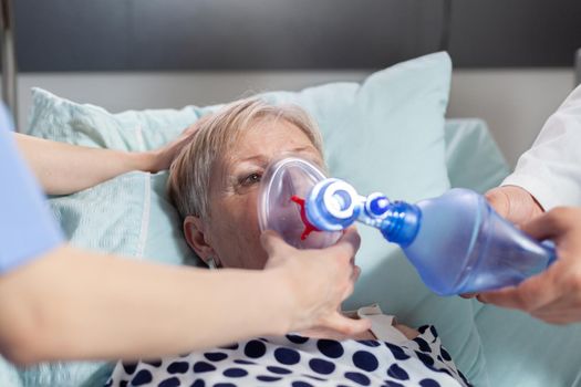 Close up shot of sick senior woman inhale and exhale with help from medical staff using ambu bag, during resuscitator for ventilation of patient. Cardiopulmonary resuscitation process.