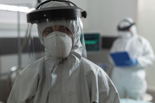 Medical specialist with face mask dressed in coverall, during coronavirus pandemic outbreak , to prevent infection with covid-19. Doctor taking notes on clipboard talking with patient.