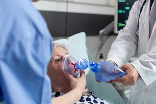 Doctor and nurse helping sick hospitalized senior woman breath, with ambu bag during resustacitor process, due to lung infection, iv drip bag attached. Cardiopulmonary resuscitation process.