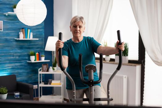 Active retirement senior woman working legs muscle using cycling bicycle machine watching fitness video on television for well being. Pensioner doing body exercise during health cardio workout