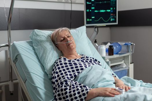 Elderly patient following recovery treatment laying in hospital bed, getting intravenous medicine from iv drip bag. Breathing through oxygen tube because of pulmonary failure.