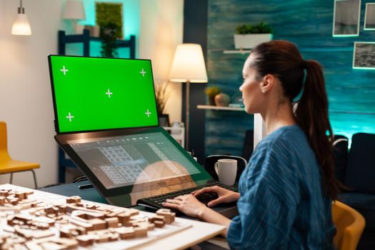 Engineer architect using green screen and blueprint on monitor computer screen at workplace. Woman doing manufacturing work on software template for chroma key mockup development project