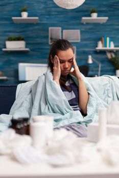Sick woman with headache sitting on sofa at home, taking pills and medical treatment for cold flu pain fever. Person with disease and health issues having migraine and suffering of virus symptoms
