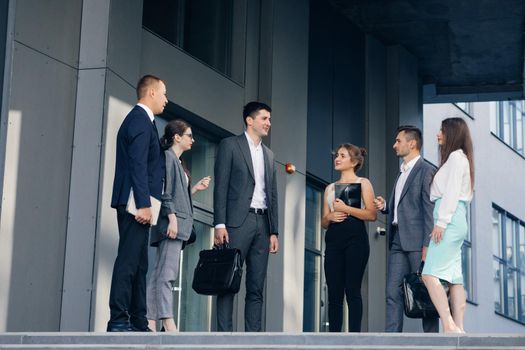 Confident team members on stairs. Business men and women in formal suits talk on the background of modern office building. Male and Female Business People Discuss Business. Group of six people