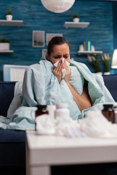 Ill woman suffering from coronavirus symptoms at home with medical treatment against sickness. Young person resting with infection flu illness sickness disease using tissues