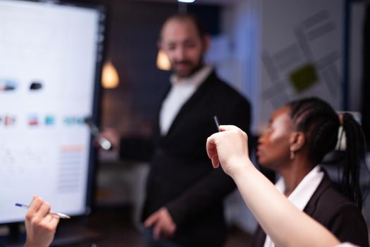 Selective focus of businesswoman asking question during branstorming, late at night in the office. Diverse teamwork working at management presentation in meeting room.