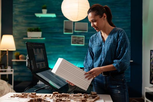 Engineer person holding maquette at layout desk for building plan and construction model concept. Caucasian woman using architectural design for measurement technology blueprint project