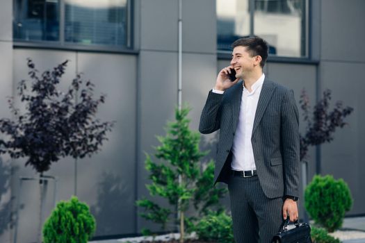 Confident Businessman in Classical Suit Talking on Smartphone and Walking in Street. Young Business Man Having Business Conversation
