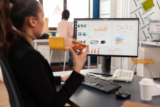 Businesswoman enjoying food meal order in company office during takeout lunchtime break working at financial graphs. Entrepreneur woman eating takeaway delivery pizza slice at desk