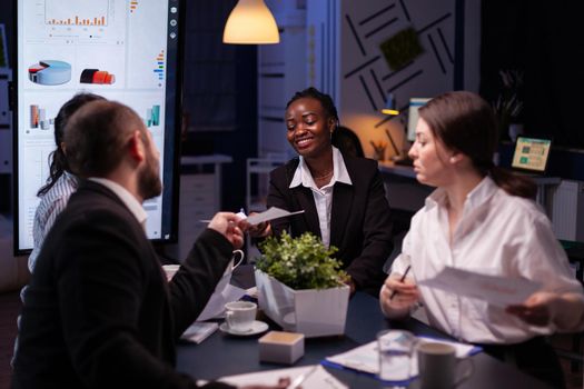 Diverse multi-ethnic businesspeople overworking late at night analyzing management ideas solving company statistics. Workaholics teamwork working in office meeting room in evening..