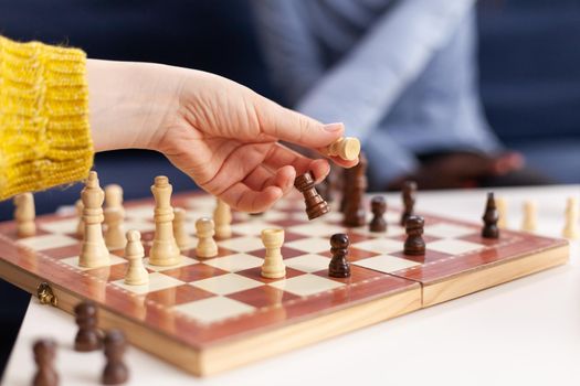 Close up of woman moving chess pieces on board during global pandemic with coronavirus. Group of friends having fun in home living room. Conceptual image. Board games, competing, tactics, asctivity.