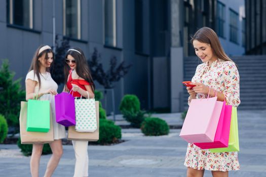 Happy shopping woman with a group of friends at the background. Retail, gesture and sale concept. Smiling teenage girl with many shopping bags at mall