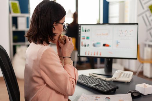 Businesswoman working in startup company office having food meal takeout lunchtime eating tasty sandwich slice typing marketing strategy. Takeaway fastfood order delivered at work place.