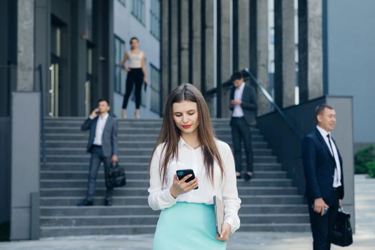 Caucasian Confident Young Business Woman is Using Smartphone App Outside near Modern Office Building.