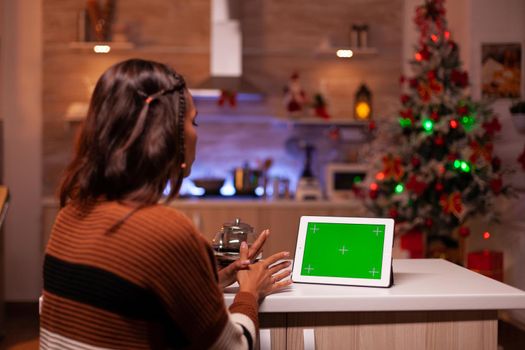 Young person watching green screen technology on tablet in kitchen at home. Caucasian woman using digital chroma key concept for background template, mockup gadget app on virtual display