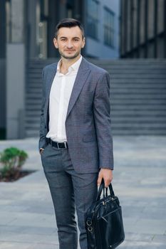 Portrait of a handsome businessman standing outdoors near office building. Businessman with suitcase.