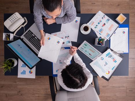 Top view of office workers meeting analyzing financial charts holding clipboard. Manager and employer discussing marketing strategy during briefing. Pointing at graphs.