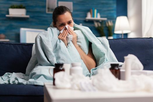 Ill woman suffering from coronavirus symptoms at home with medical treatment against sickness. Young person resting with infection flu illness sickness disease using tissues