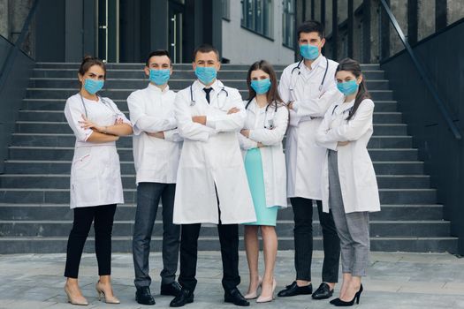 Group of doctors with face masks looking at camera, corona virus concept. Confident team of doctors in face masks standing with their arms folded and looking at camera.