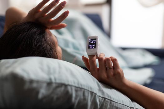 Woman at home using medical oximeter equipment to measure oxygen saturation. Pulse oximeter showing low oxygen saturation. Patient with covid in quarantine resting, measuring blood oxygen level.