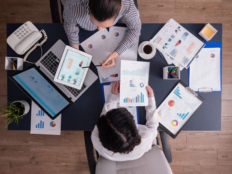 Top view of manager explaing financial strategy to employee sitting at desk in corproate office, pointing at charts on clipboard. Coworkers during briefing in start up company.