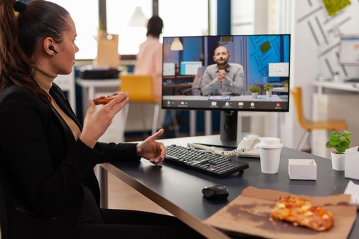 Manager woman discussing with remote entrepreneur during online videocall meeting conference having delivery lunch meal break . Businesswoman eating pizza and drinking coffee at desk in company office