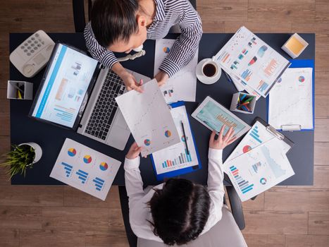 Top view of corporate business people doing good teamwork, working on financial stratey, looking at chart on paperwork, sitting at desk. Marketing team using tablet pc and laptop with documents.