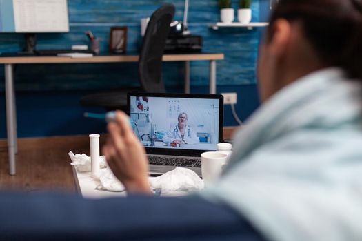 Woman on computer webcam consultation with doctor sitting at home. Young patient with cold flu illness fever temperature virus calling for support medicine diagnostic and medications