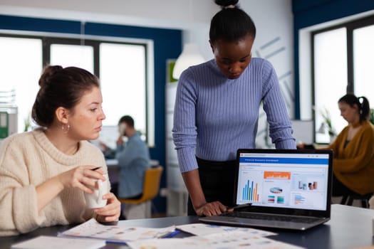 Diverse team of financial company working together on corporate charts and statistics. Multiethnic employees gathered in co-working space of startup new business.