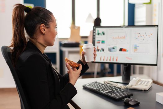 Businesswoman having delivery food order on desk during takeout lunchtime working in business company office. Entrepreneur woman eating takeaway lunch pizza slice management statistics.