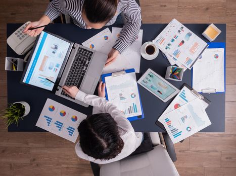 Top view of corporate business people doing good teamwork, working on financial stratey, looking at chart on paperwork, sitting at desk. Marketing team using tablet pc and laptop with documents.