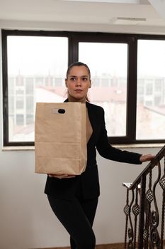 Entrepreneur woman climbing stairs in startup company office holding takeaway food meal order during takeout lunchtime. Delivery guy bringing fastfood lunch order package to businesswoman client
