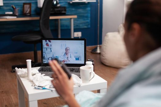 Cold young woman calling doctor from computer to treat flu illness virus fever temperature. Patient with thermometer on online consultation for treatment pills diagnostic assistance