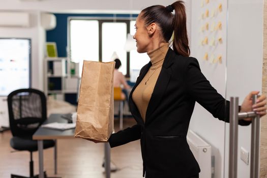 Entrepreneur opening glass at corporate business office holding lunch meal takeaway food. Corporate businesswoman with paper bag having delicious fast food takeaway deliverd by guy.