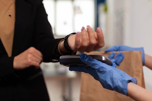 Businesswoman paying takeaway food meal order with smart watch using POS contactless terminal service during takeout lunchtime. Delivery guy bringing tasty lunch deliver at workplace