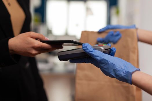 Close up of businesswoman paying takeaway food lunch order with smartphone using POS contactless service during takeout lunchtime at company workplace. Delivery guy bringing fresh meal.