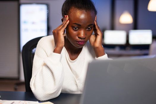 Exhausted african entrepreneur analysing financial revenues laptop working overtime. Stressed employee using modern technology doing overtime for deadline of project.