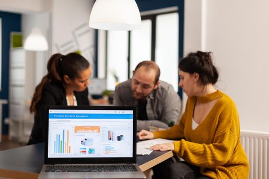 Business woman talking about financial project, taking notes, discussing start up ideas using laptop. Diverse employees gathered in co-working, working process in busy company, teamwork help concept