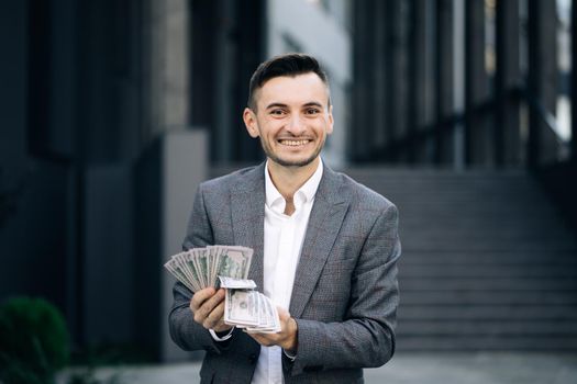 Man shows money and celebrating success, victory while looking to camera. Amazed happy excited businessman with money - U.S. currency dollars banknotes.