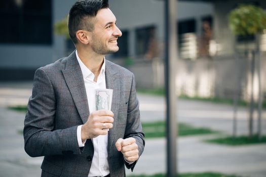 Happy rich successful man holds dollars outdoors. Portrait of satisfied businessman holds money. Lifestyle, richness, joy, success.