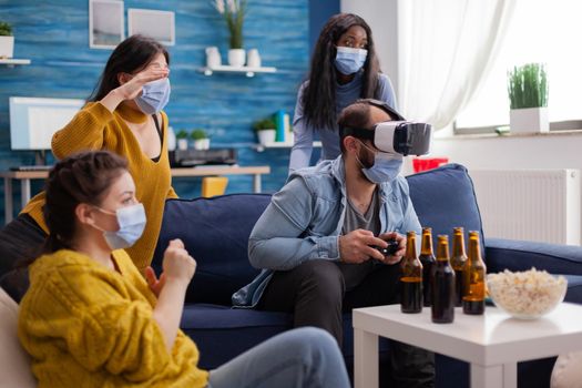 Woman experiencing virtual reality playing video games with vr headset wearing face mask while friends are cheering up keeping social distancing wearing face mask to prevent infection with virus, Beer bottles, Conceptual image.
