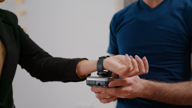 Closeup of businesswoman making contactless payment with smart watch using POS terminal service. Delivery guy worker bringing takeaway food meal order during lunchtime in company office